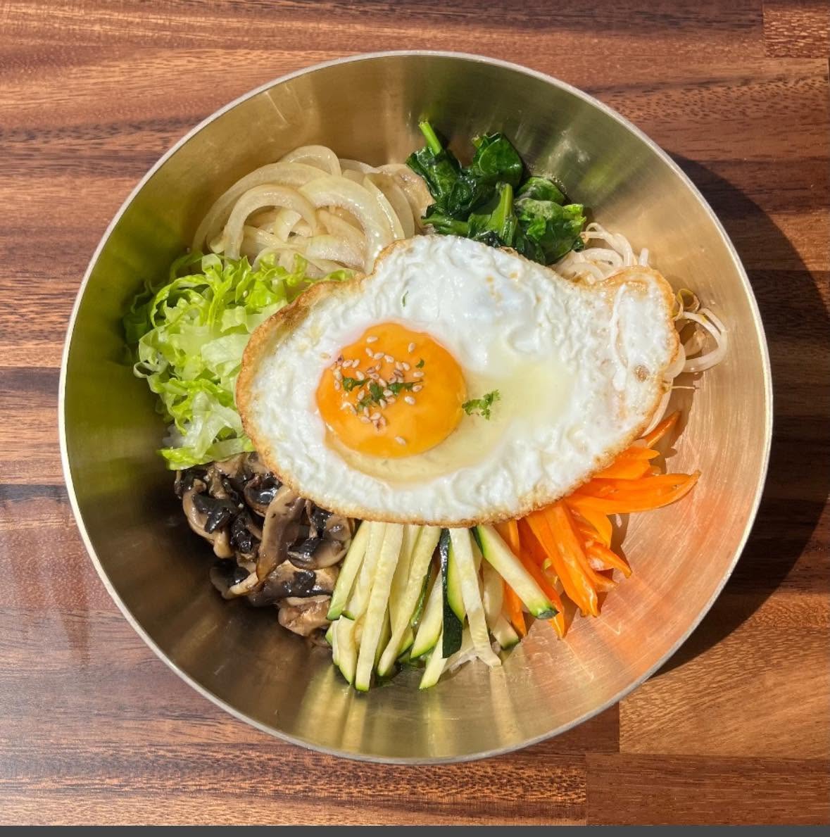 Bibimbap rice bowl topped with a fried egg, vegetables and sesame seeds in a brass bowl
